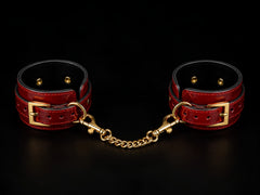 The Scarlet Cuffs crimson vegan leather wrist and ankle restraint set with adjustable straps and polished gold-tone hardware.